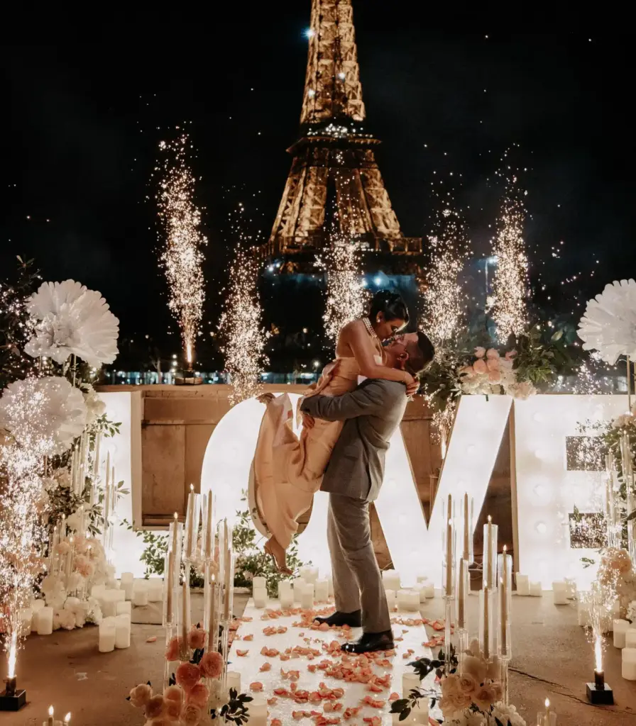 Breathtaking nighttime proposal in Paris featuring a couple embracing in front of giant 'LOVE' light letters, glowing candles, sparkling cold sparks, and the illuminated Eiffel Tower