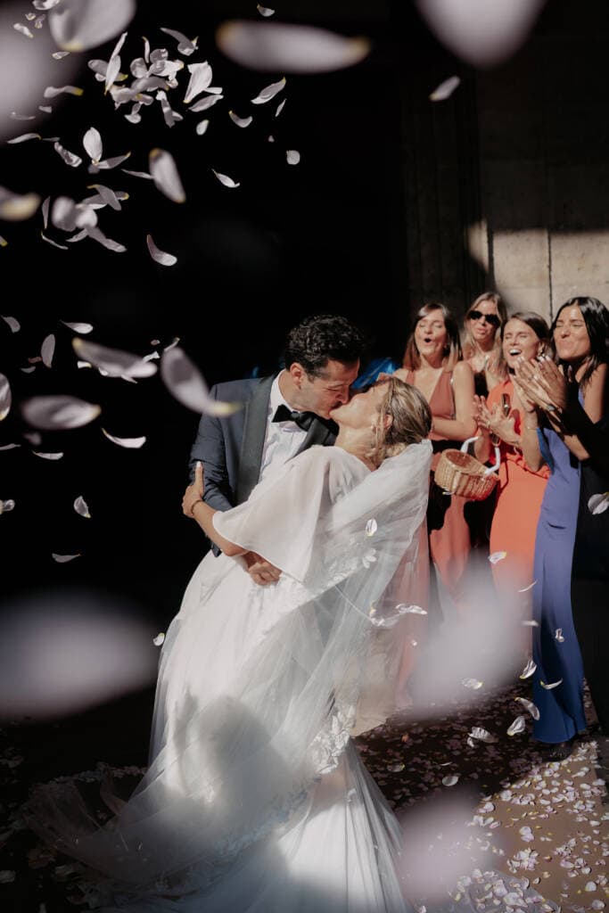 Romantic bride and groom kiss with flower petals toss organized by luxury wedding planner in Paris